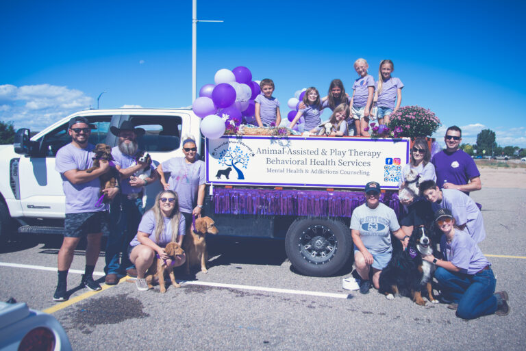 A team of employees poses in front of a truck used as a parade float with signage for Peaceful Paws Therapy